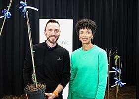 Daniel Lüttger hält einen Apfelbaum in der Hand, daneben steht Olympiasiegerin Malaika Mihambo