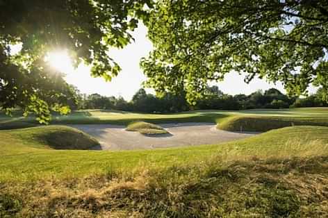 Golfbunker bei Sonnenschein mit grüner Wiese im Vordergrund
