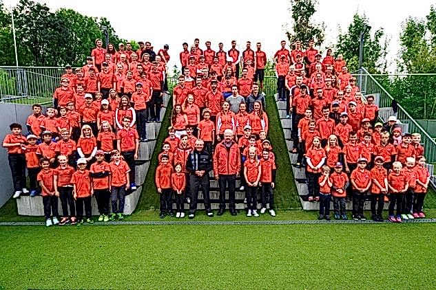 Ehrenpräsident Dietmar Hopp steht mit 100 Kindern auf dem Athletikplatz auf einer Treppe