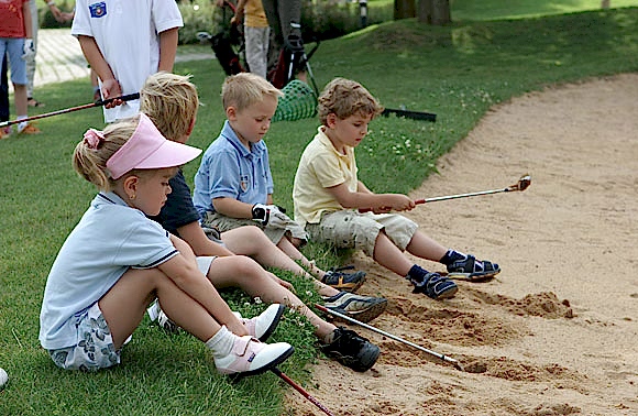Vier Kinder sitzen im Bunker und halten Golfschläger